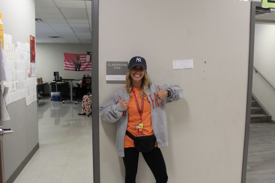 Person in orange shirt and cap stands against wall in a hallway. A flag and papers are on the wall.
