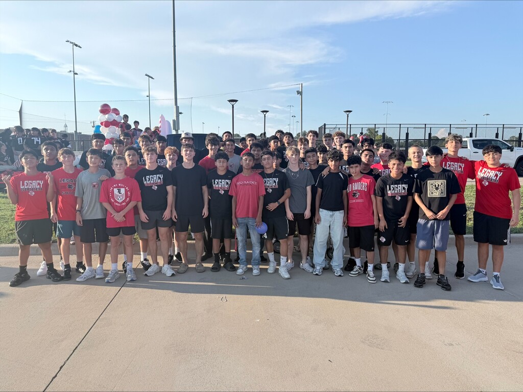 Group of people in sports gear stands in a line outdoors, some wearing red shirts and others wearing black.
