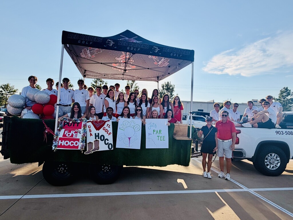 Group of people in a school float with a canopy. Two adults stand in front, others behind them. Red and white banners and balloons in the float.
