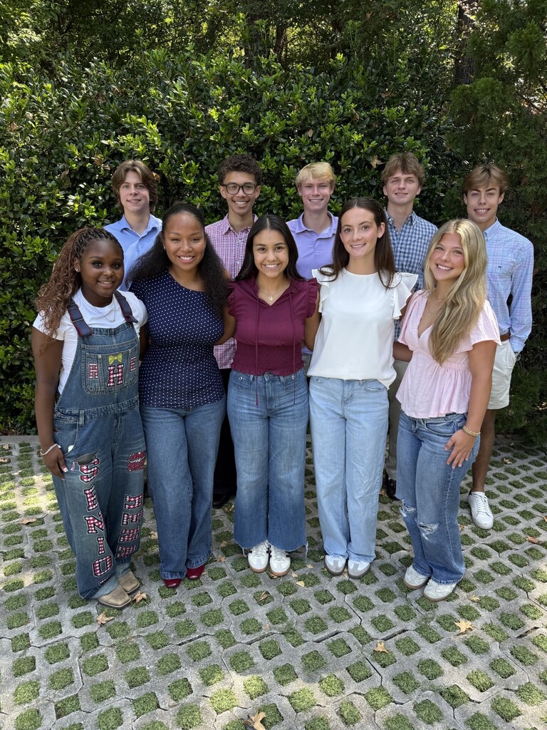 A group of young individuals in casual attire, including jeans and shirts, stands together in an outdoor area.