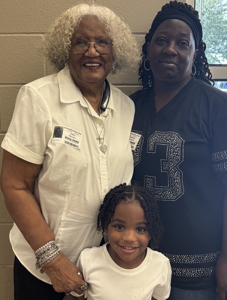 Three women stand together, smiling. A young girl between two adults, one wearing a white shirt, the other a black shirt with number 3.