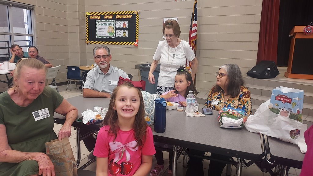 A young girl, center, sits with her grand mother, while a famly in the back ground visits at a table.