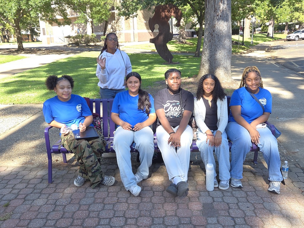 Group of young people in blue shirts pose for photo on a bench in a park.