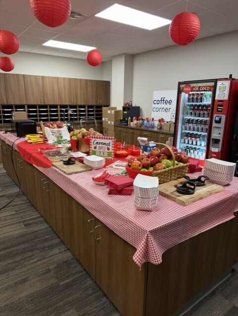 Long table with fruit, bowls, plates, and a coffee machine. Red and white tablecloth, red lanterns hanging from ceiling.