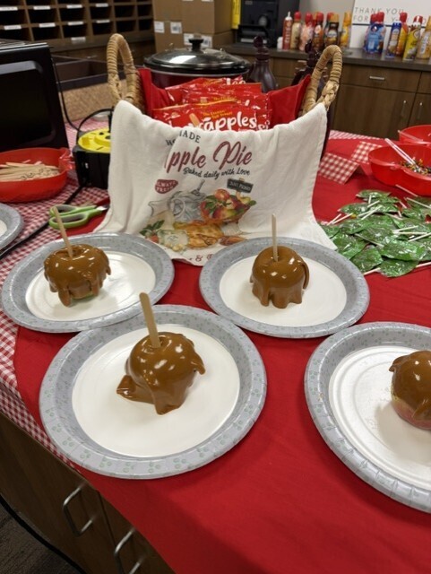 Four plates of caramel apples on a red tablecloth. One plate has a brown apple.