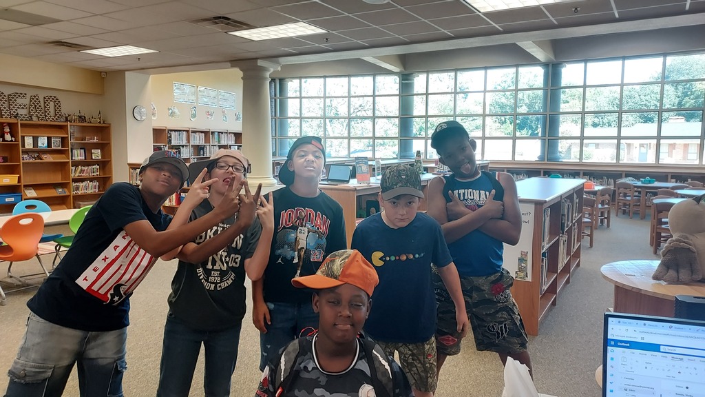 Five children in casual wear pose for a photo in a library, standing in a row.