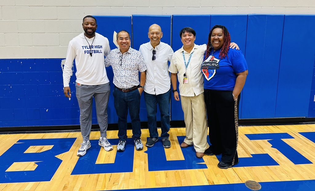 Five adults stand on a basketball court. One wears a blue shirt with the word "Bulls" on it.