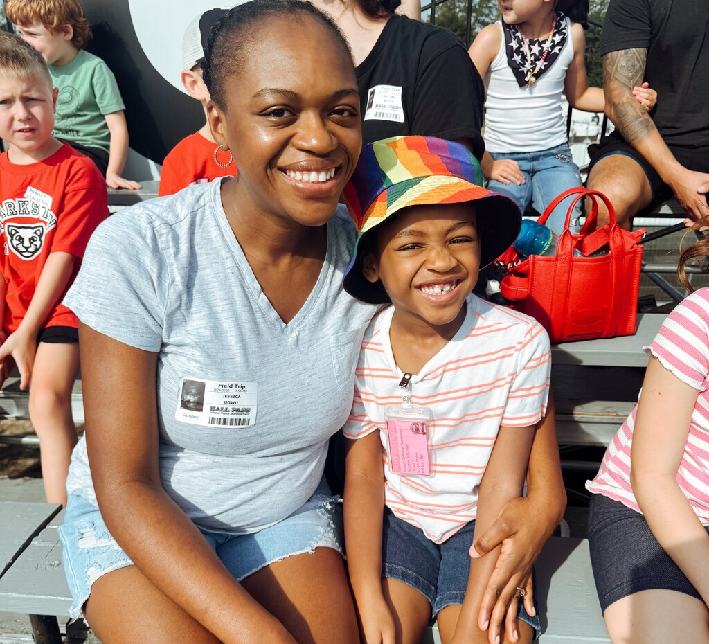 Woman and child in red and white striped shirt sitting on bleachers with other children.