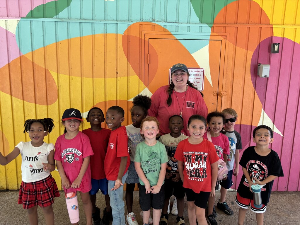 A group of Mrs. Lechner's students, some wearing hats and sunglasses, poses for a photo in front of a colorful mural.