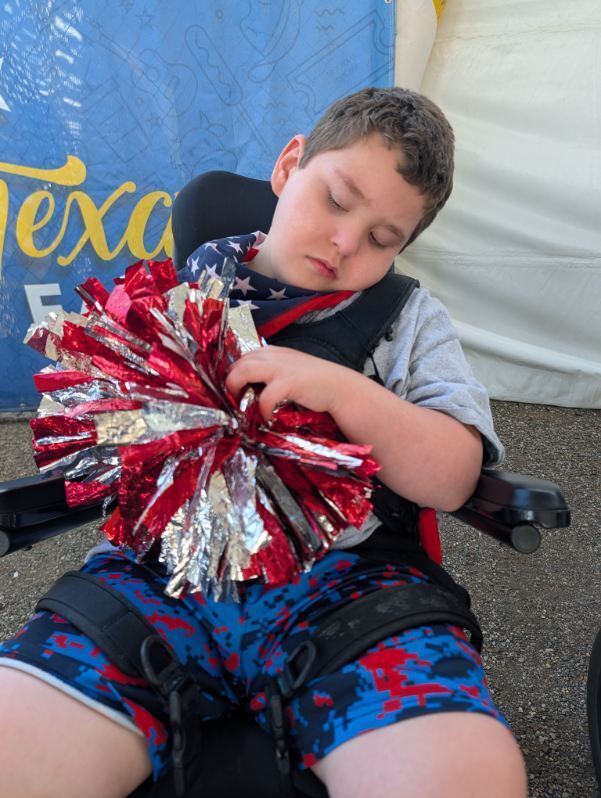 student in wheelchair with Boshears wheelchair dance team t-shirt on and holding a pom pom
