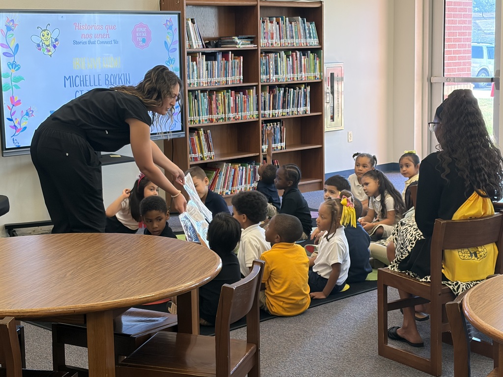 A woman reads a book to a group of children sitting on the floor in a library.