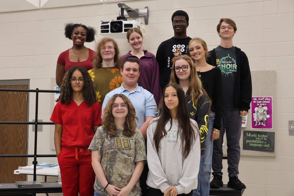 A group of young individuals in various colors and styles of clothing stand together indoors.