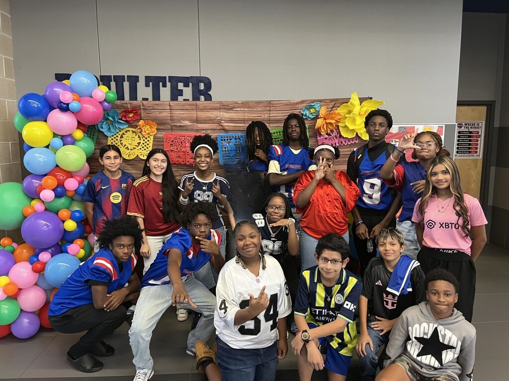 Group of young people, some wearing sports jerseys, posing for a photo in front of balloons.