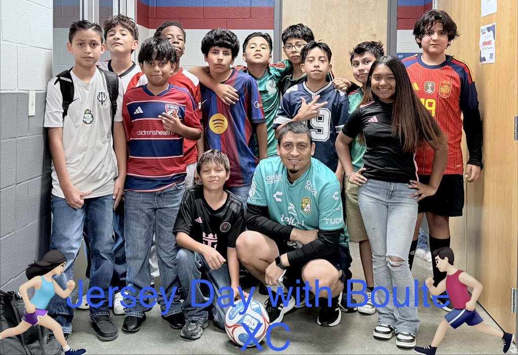 Group of children and two adults in sports jerseys, posing for a photo in a corridor.