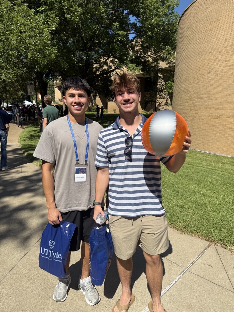 Two men on a sidewalk. One holds a beach ball, and the other carries blue bags.