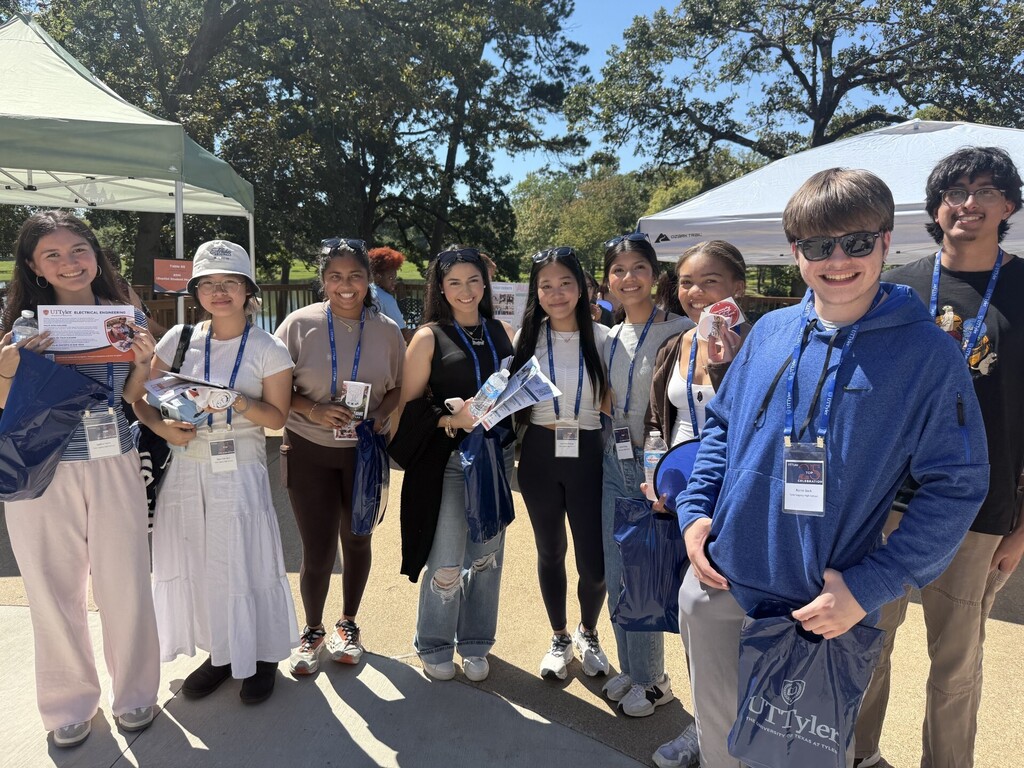 A group of people wearing name tags, smiling, and standing under a tent. Some are holding items.