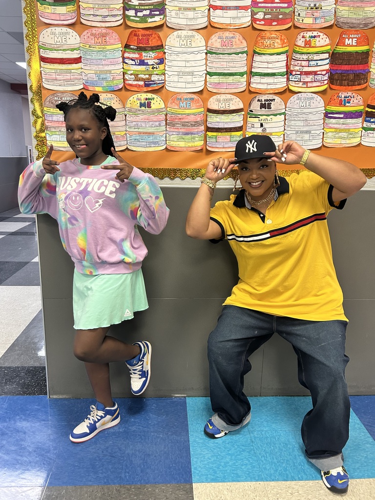 Two children posing in front of a bulletin board displaying various colorful items.