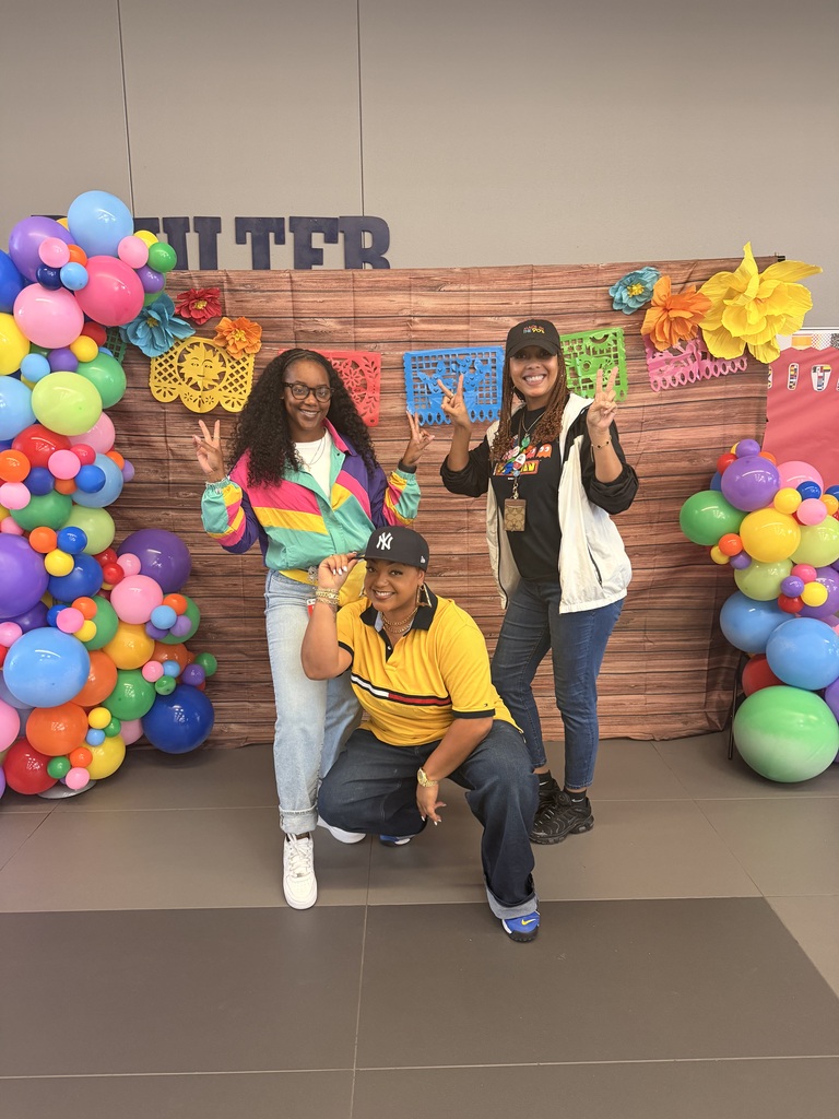 Three individuals are posing for a photo against a backdrop of colorful balloons and festive decorations.