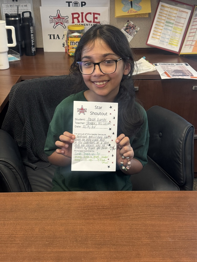 student sitting at the principals desk holding up a certificate