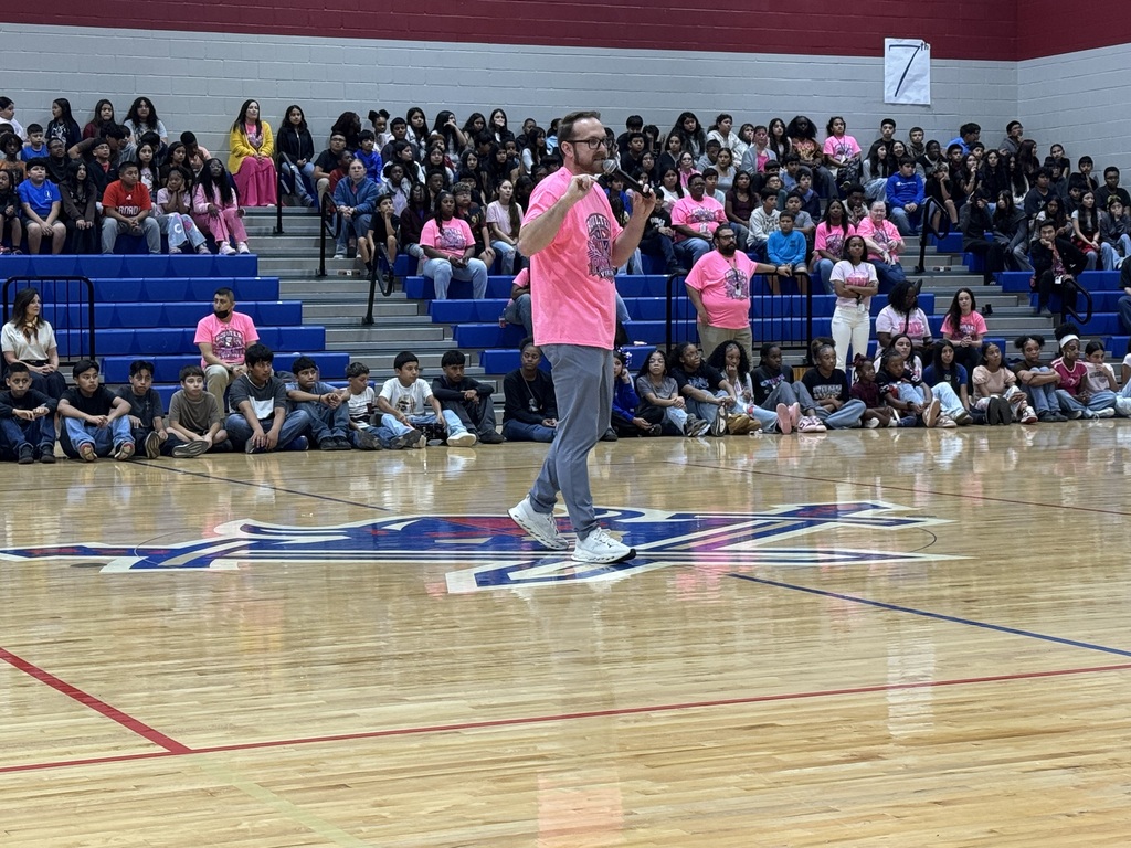 A man walks on a basketball court while a crowd sits on bleachers. The court has a logo in the middle.