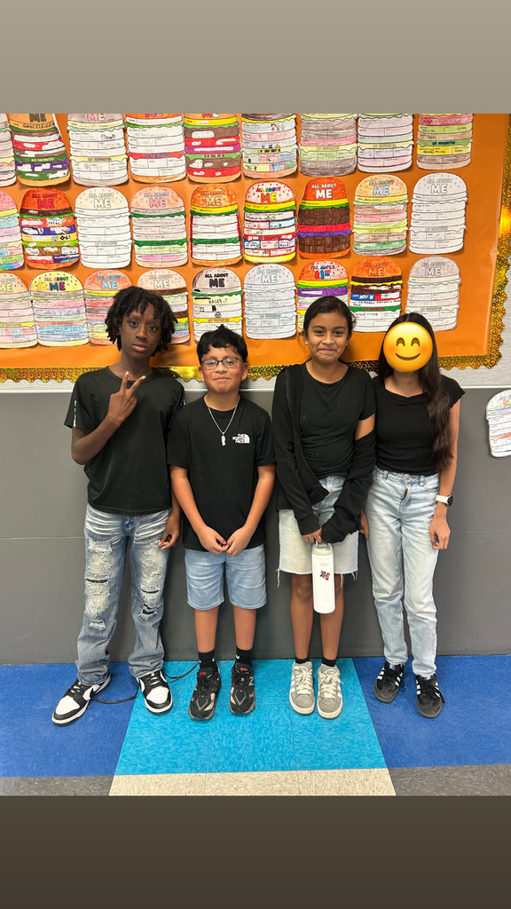 Four children in matching black t-shirts pose against a wall with a colorful hamburger display.