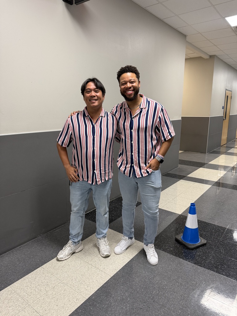 Two men in matching outfits, standing next to each other in a hallway with checkered floor.