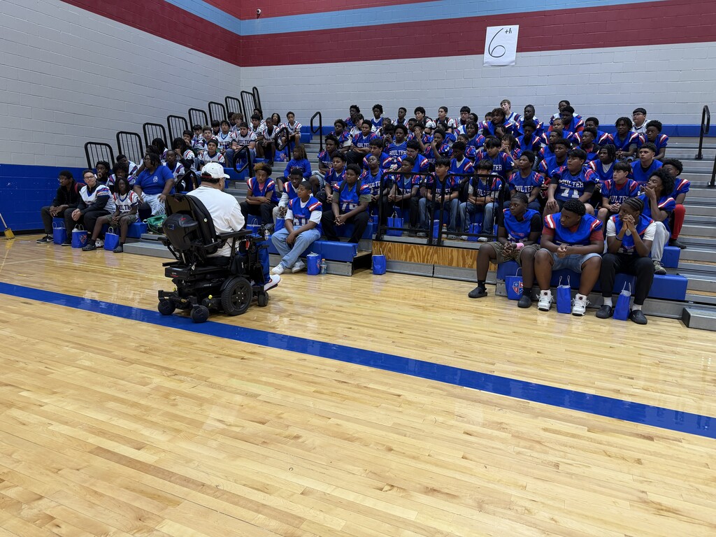 Group of students in blue uniforms seated in bleachers, with Nico Herndandez in a wheelchair in front.