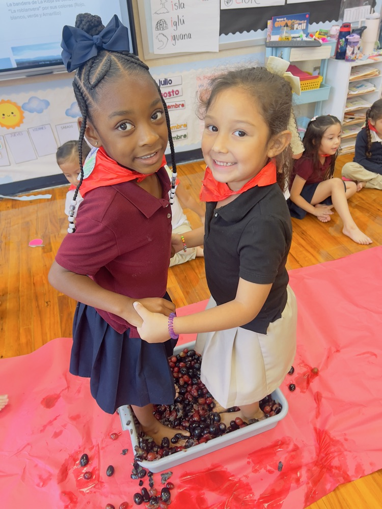 two girls in uniform dresses, stepping on grapes and a gray bucket