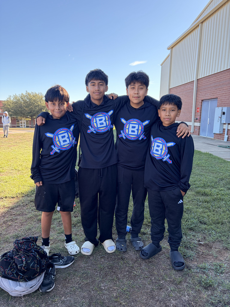 Four boys in matching black jerseys with blue designs stand together on a field, backpacks on the ground.