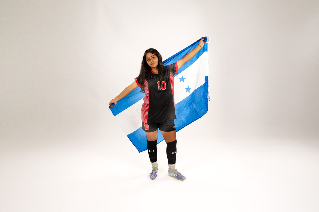 Person wearing soccer uniform holding a flag of Honduras, standing with arms extended over head.