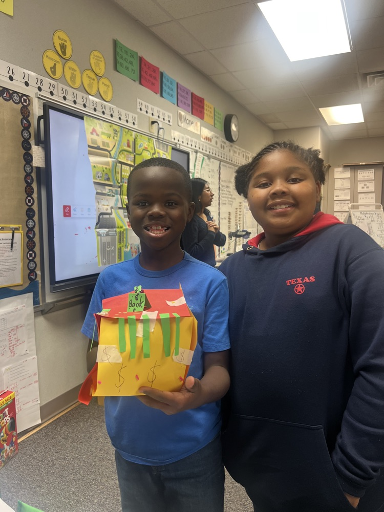 Two students, one holding a gift box, stand in a classroom with a whiteboard, bulletin board, and clock in the background.