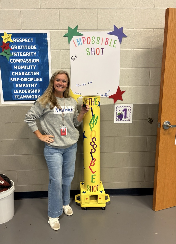 A woman stands by a yellow and white pole with "The Impossible Shot" and a poster.