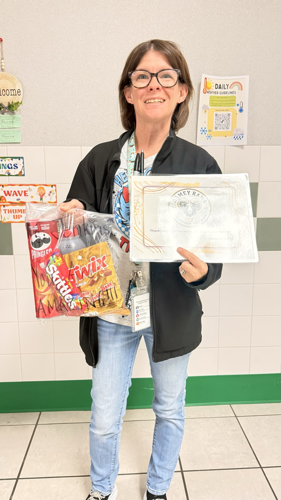 Person standing in a hallway holding a bag of chips, a certificate, and a pen.