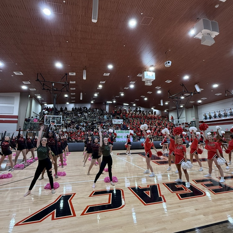 Cheerleaders performing on a basketball court with a large crowd watching from bleachers.