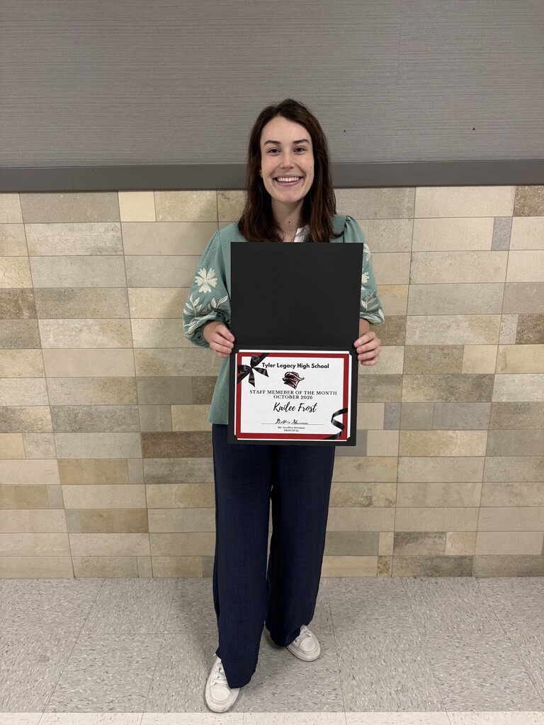 Person holding black folder with red and white paper, smiling for photo. Tiled wall behind.