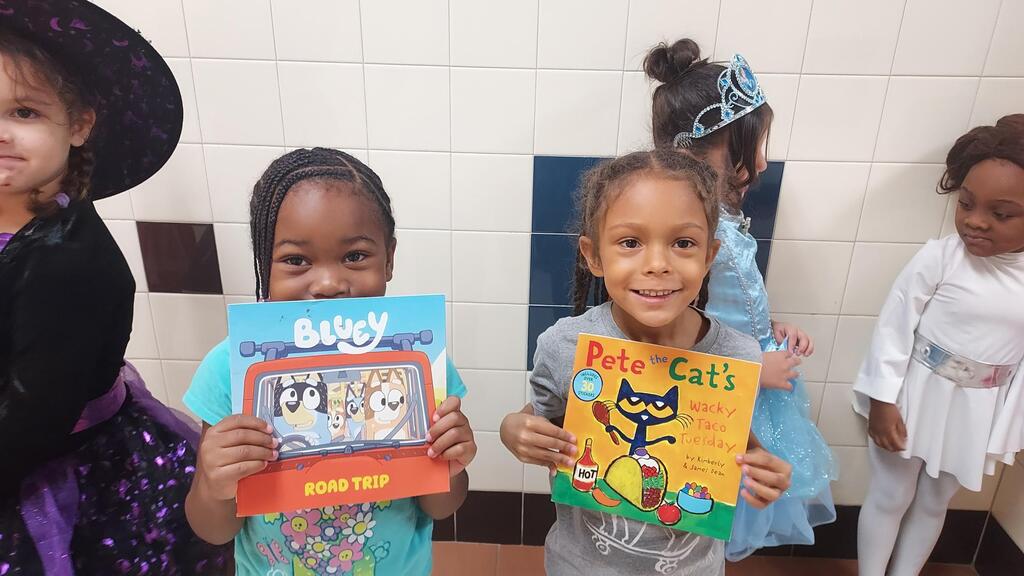 Children dressed in costumes hold books; one holds "Bugsy" and another holds "Pete the Cat".