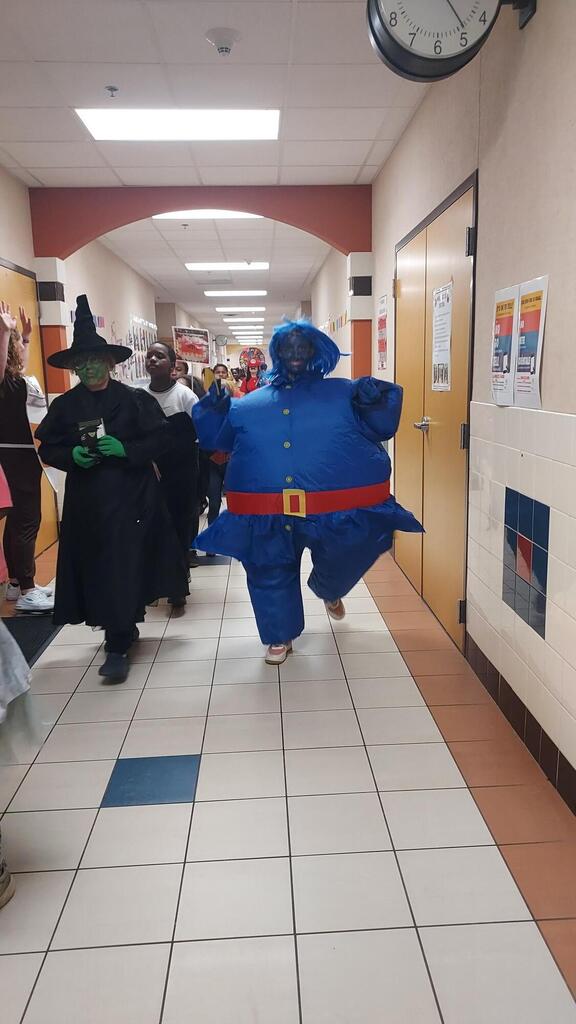 Two students walk down a hallway in costumes. One is dressed as a witch; the other as a balloon.