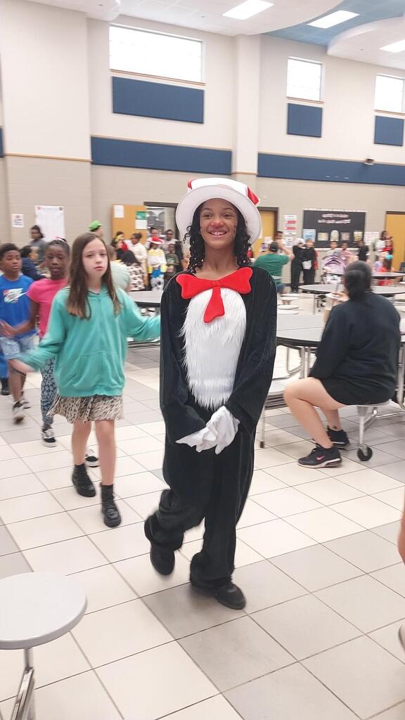 A person in a Dr. Seuss Cat in the Hat costume walks in a school cafeteria.