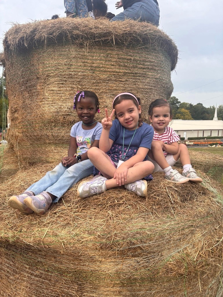 Three children sit on a large hay bale. The girl in the middle makes a peace sign.