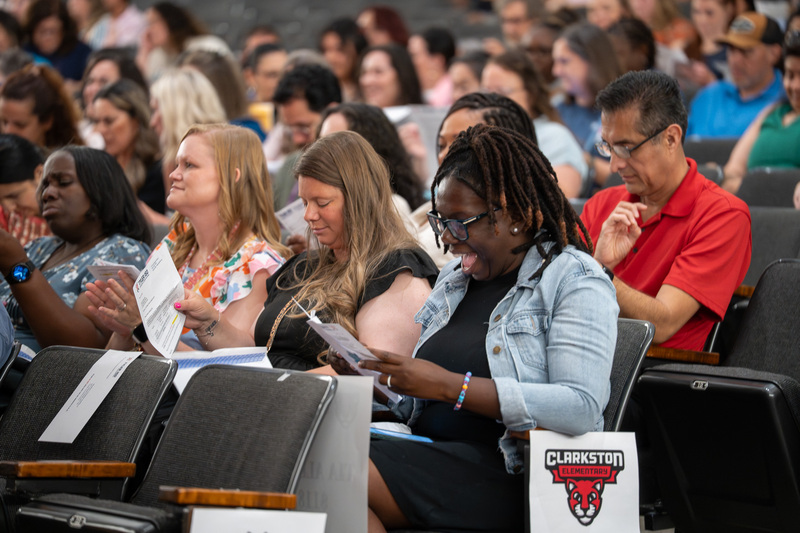 men and women sitting in chairs opening envelopes with surprised expressions
