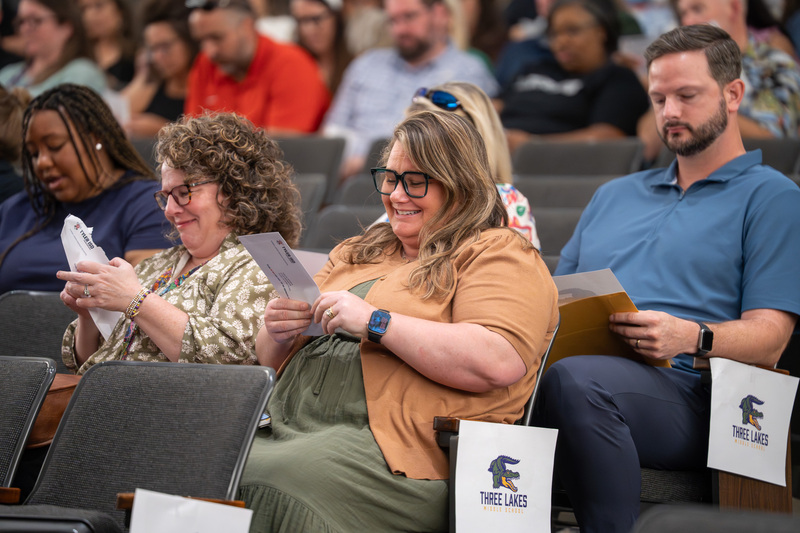 men and women sitting in chairs opening envelopes with surprised expressions