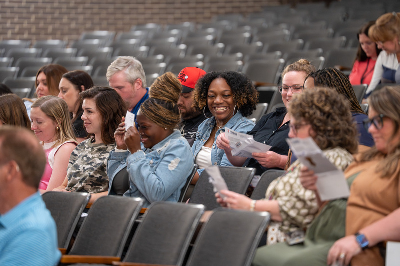 men and women sitting in chairs opening envelopes with surprised expressions