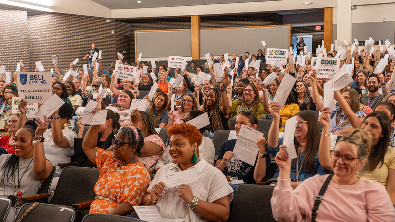 men and women sitting in chairs holding up envelopes, papers, and checks in the air