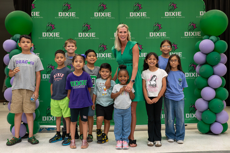 woman standing with group of children in front of green banner with balloons