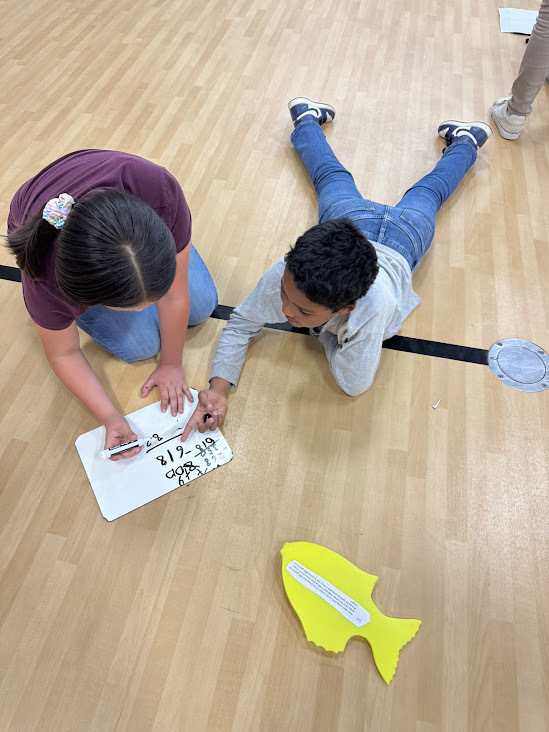 elementary kids laying on floor in gym looking at papers