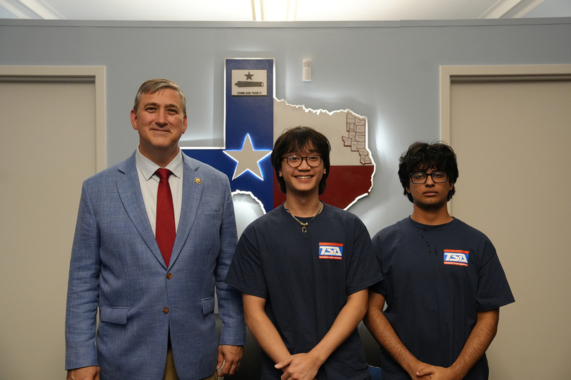 man wearing gray suit and red tie standing beside two teen boys in black t-shirts