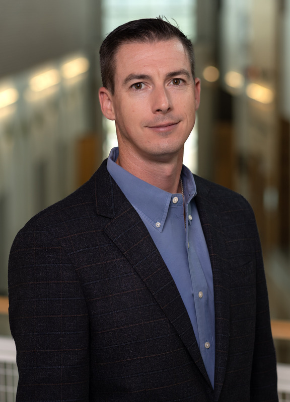 Caucasian man wearing dark jacket and blue shirt