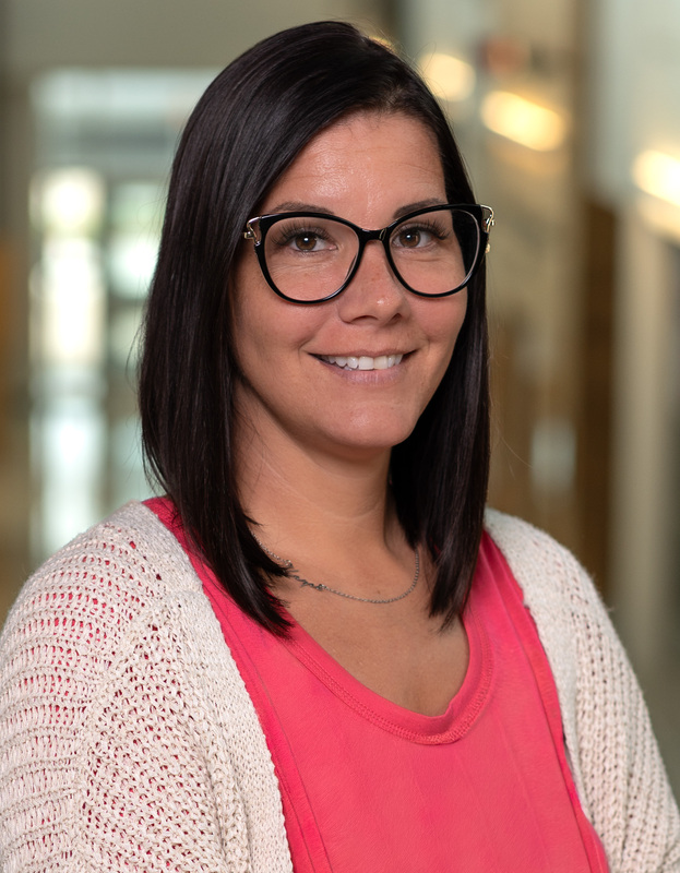 Caucasian woman with long dark hair and glasses wearing pink shirt and white sweater