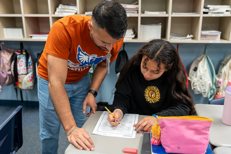 man leaning over desk with teen girl working on paper