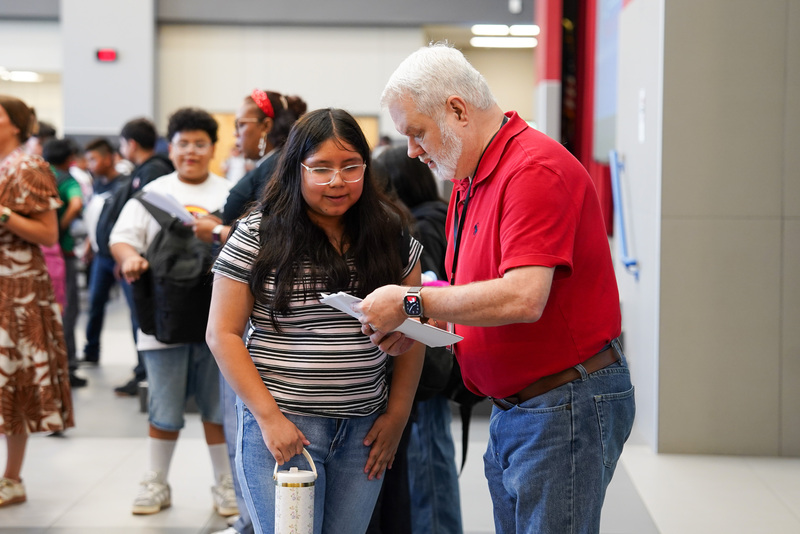 man helping teen girl in hallway as they look at a paper to see where she needs to go
